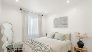 A bedroom with a bed, a vanity with a mirror, a bedside table with a vase, and a painting on the wall. - Cozy & Dreamy Getaway home ! (Montebello)