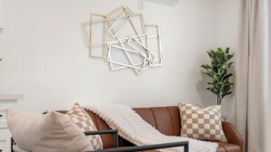 A modern living room with a brown leather sofa, white cushions, and a geometric wall art piece. - Cozy & Dreamy Getaway home ! (Montebello)