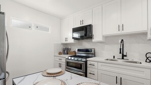 A modern kitchen with white cabinets, a stainless steel refrigerator, a microwave, an oven, and a sink. - Cozy & Dreamy Getaway home ! (Montebello)