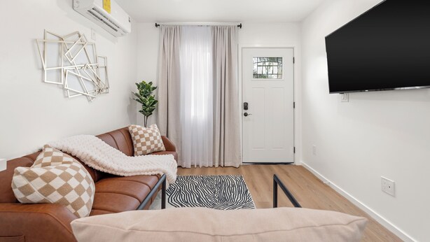 A modern living room with a leather sofa, a flat-screen TV mounted on the wall, and a door with a window. - Cozy & Dreamy Getaway home ! (Montebello)