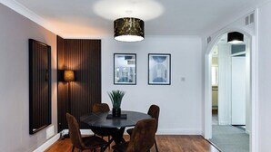 Uma sala de jantar com mesa redonda, quatro cadeiras, luminária pendente e quadros nas paredes.