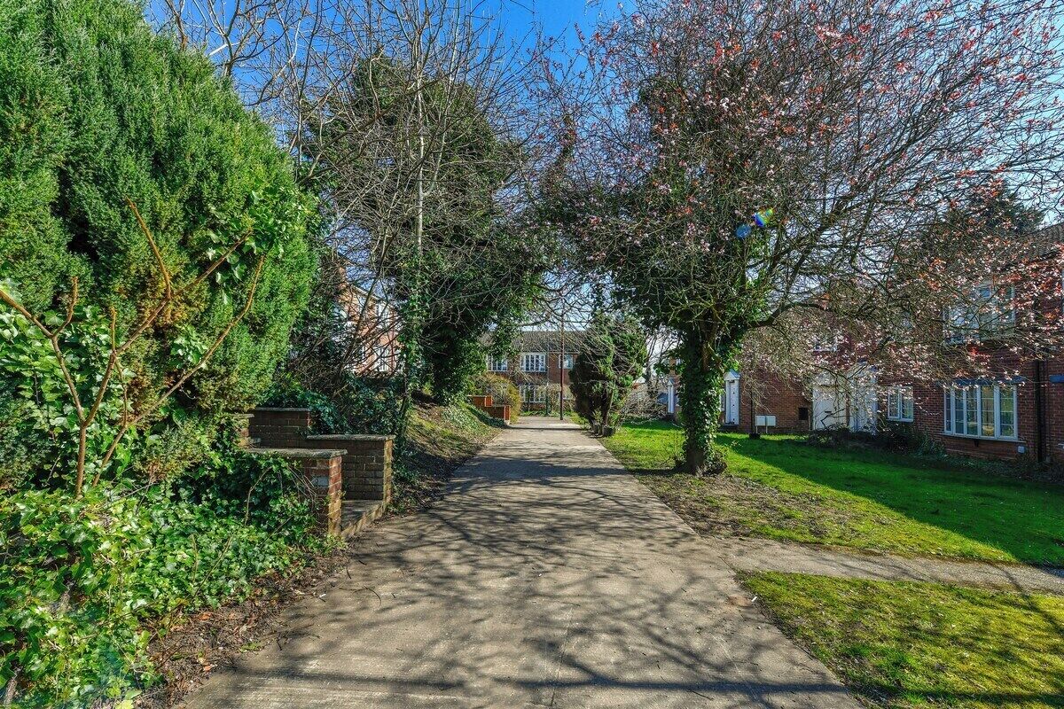 A pathway leading to a residential area with houses, a brick wall, and greenery.