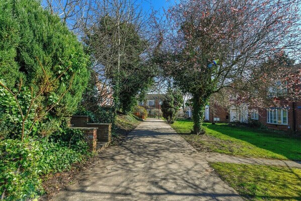 A pathway leading to a residential area with houses, a brick wall, and greenery.