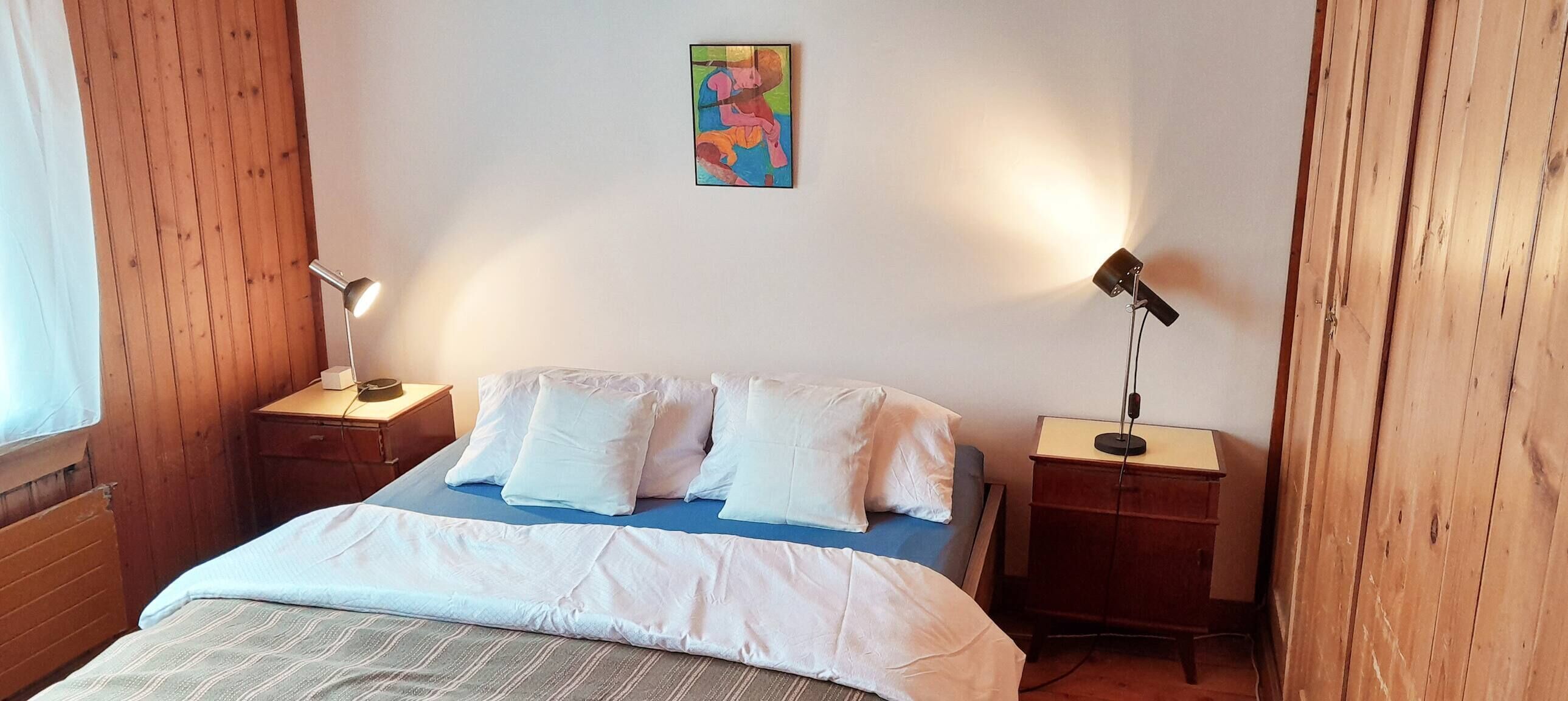 A bedroom with a bed, two bedside tables, a lamp, and a painting on the wall.