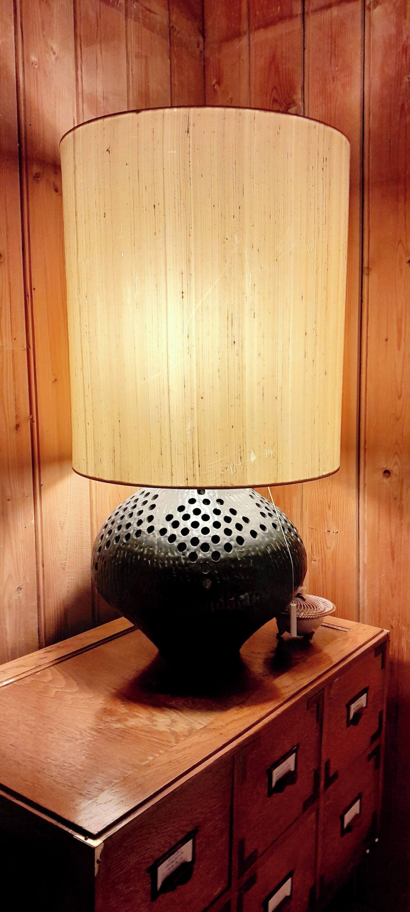 A lamp with a perforated base on a wooden table against a wooden wall.