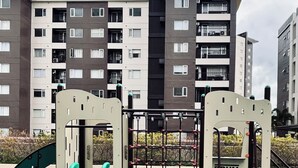 A playground with a slide and climbing structures, set against a backdrop of residential buildings.