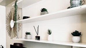 A modern living room with a flat-screen TV, white shelving units, and decorative plants.