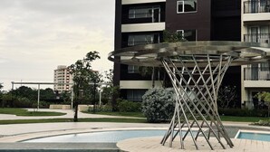 A modern apartment building with a swimming pool and a unique metal sculpture in the center.