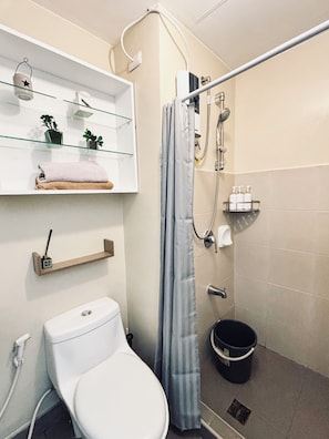 A modern bathroom with a toilet, shower, and glass shelves with towels and toiletries. - A Tranquil Hideaway in the City 332 (Iloilo)