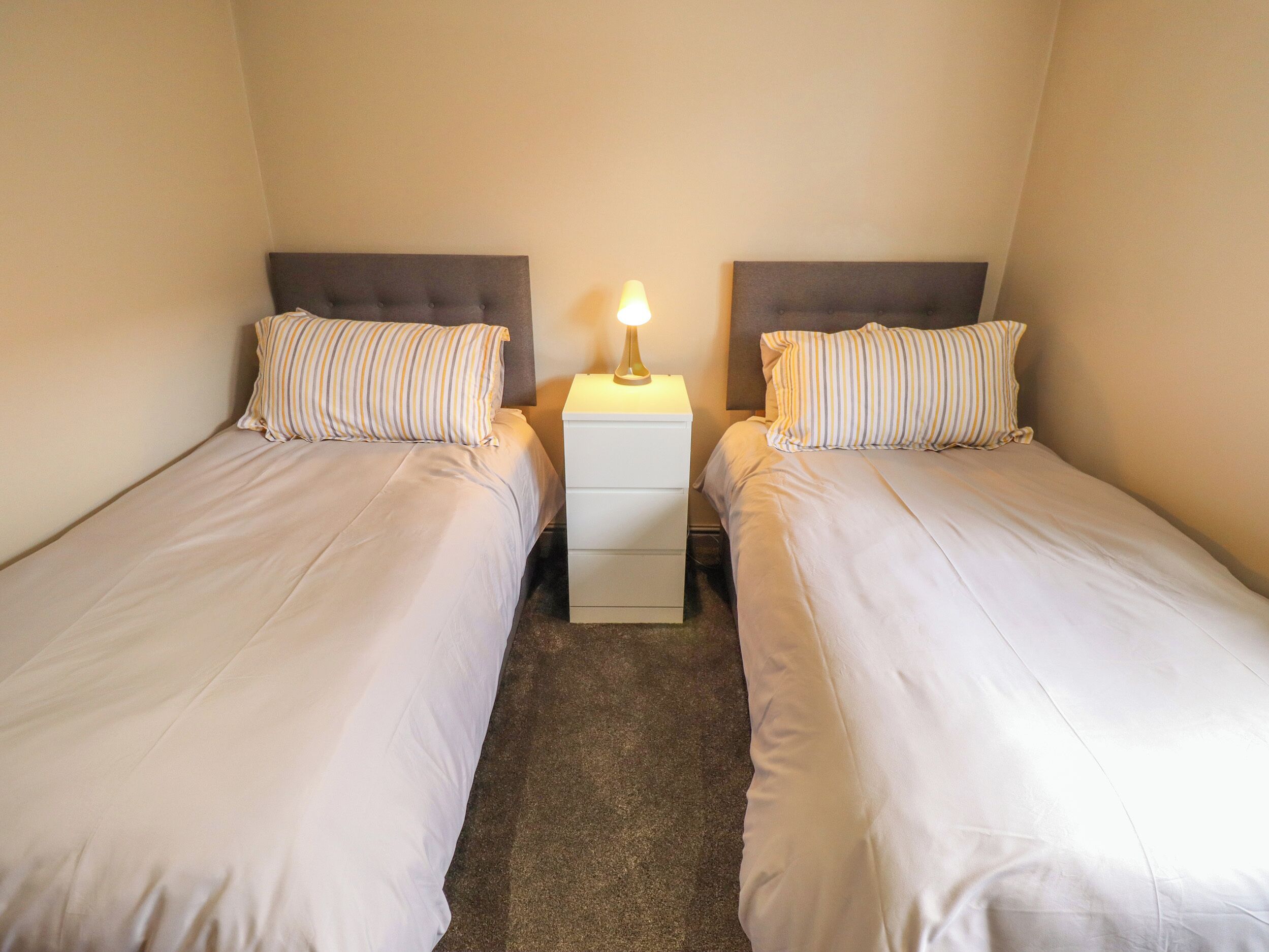 A twin room with two single beds, each with striped pillows and a bedside table with a lamp.