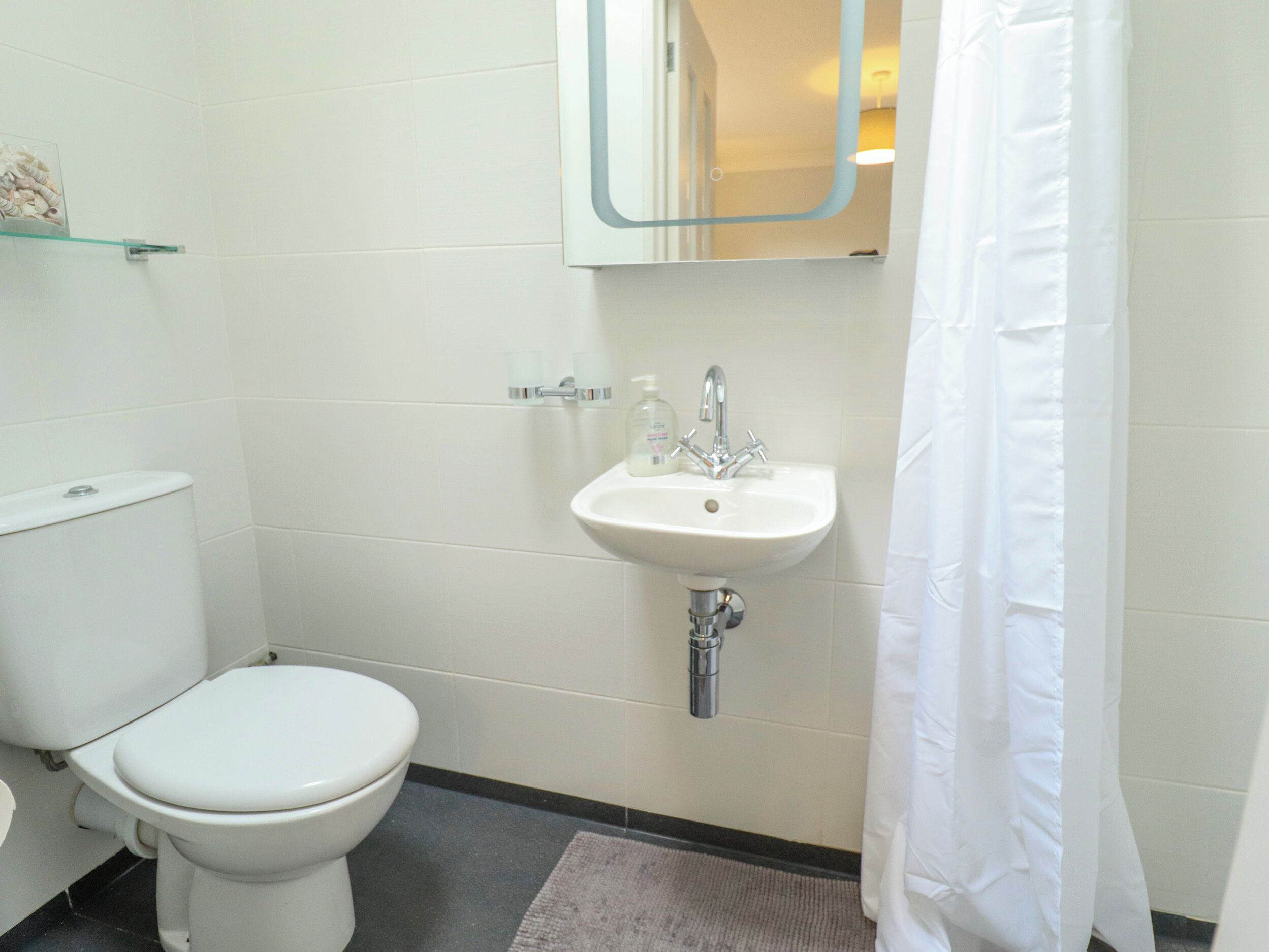 Un baño con inodoro, lavamanos y un estante de vidrio sobre el lavamanos.