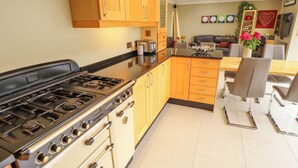 A modern kitchen with wooden cabinets, a gas stove, and a dining area with a table and chairs. - Witham View (Lincoln)