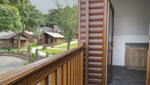 A wooden cabin with a balcony, a door leading to a room with a wooden cabinet, and a view of other cabins in the background. - Classic Lodge 15 (Rhyl)