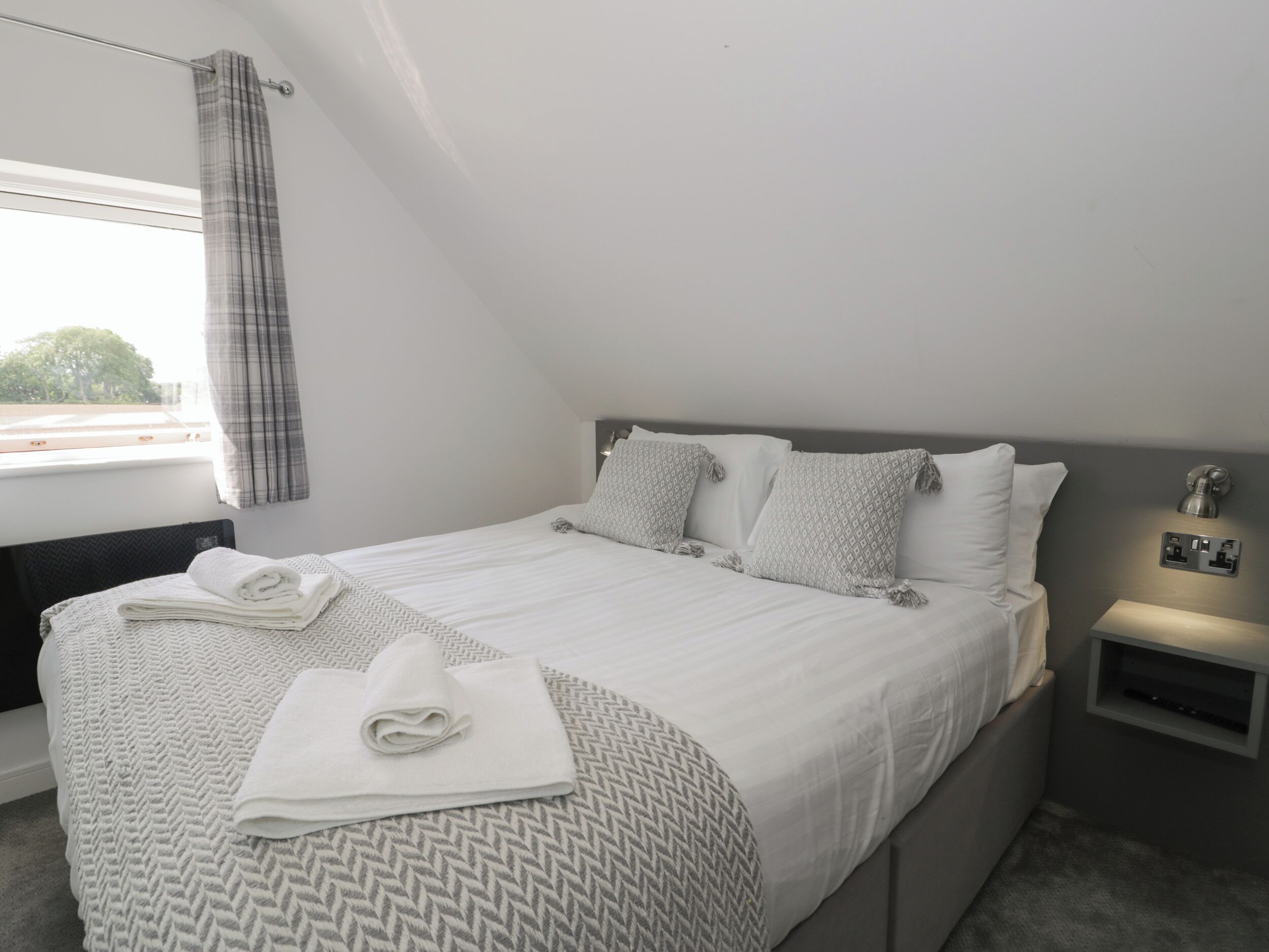 A neatly made bed with a white and gray patterned bedspread, two pillows with a geometric design, and a folded white towel on the bed.