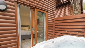 A wooden cabin with a glass door leading to a bedroom, a hot tub, and a wooden fence. - Luxury Lodge 46 (Rhyl)