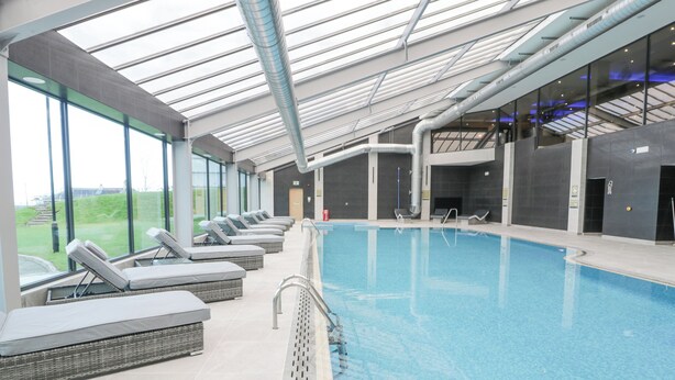 An indoor swimming pool with lounge chairs and a glass ceiling. - Classic Lodge 25 (Rhyl)