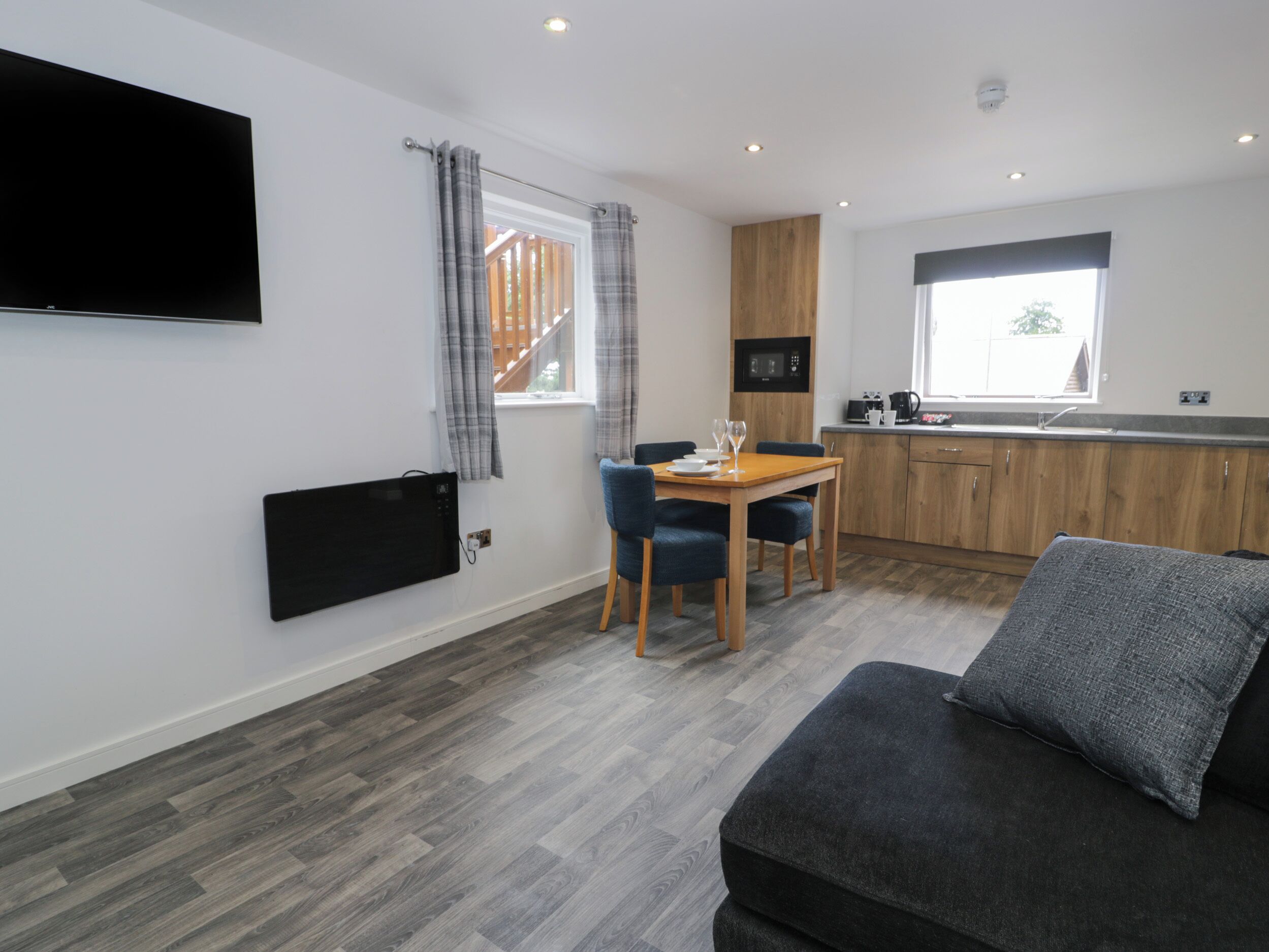 A modern kitchen with a dining area, a flat-screen TV mounted on the wall, and a window with curtains.