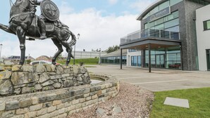 A statue of a horse and rider in front of a modern building with large windows and a balcony. - Classic Lodge 25 (Rhyl)