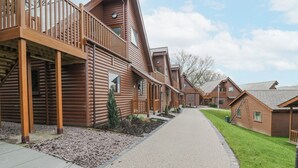 A row of log cabin-style buildings with a gravel pathway leading through the property. - Classic Lodge 25 (Rhyl)