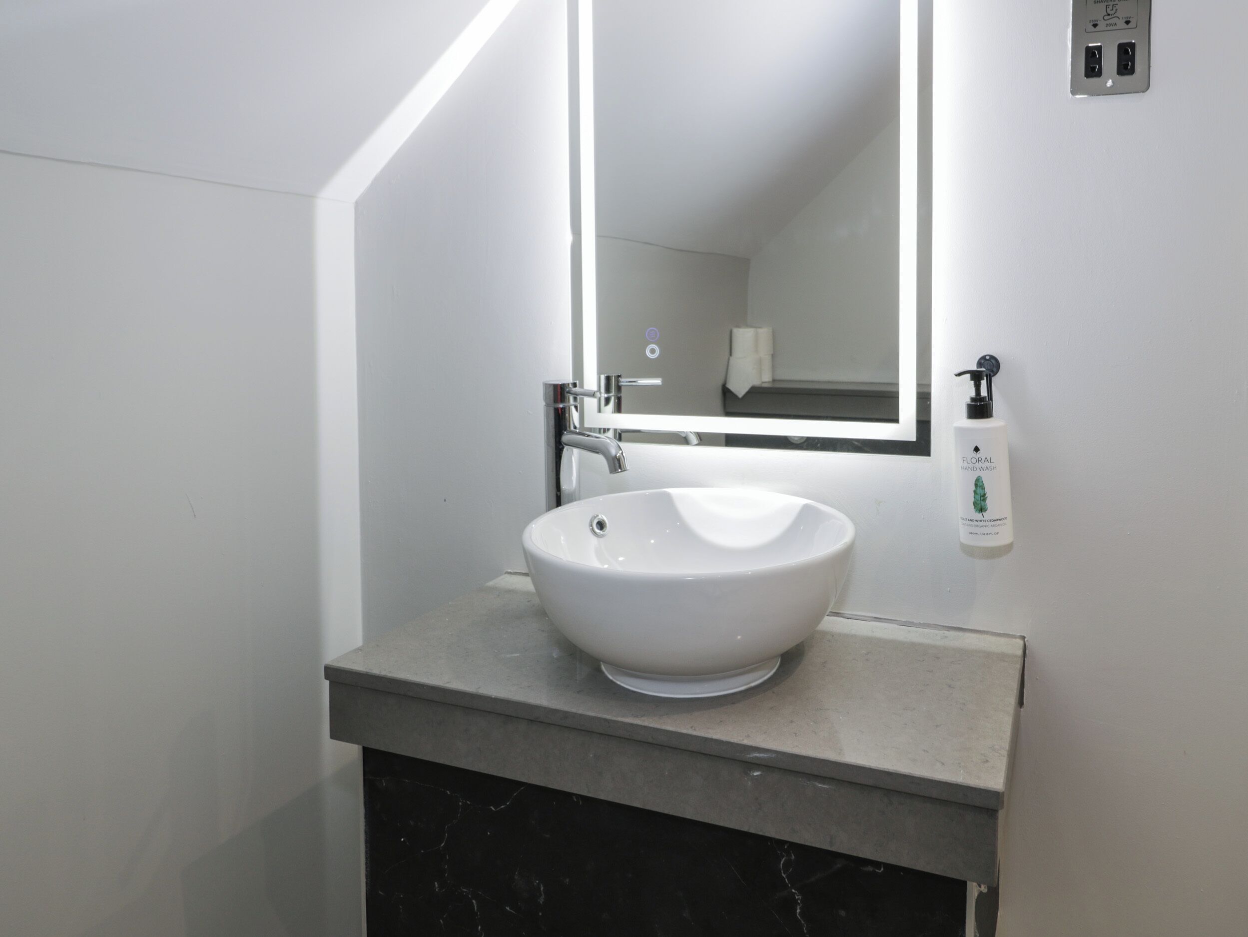 A modern bathroom with a white sink, a large mirror, and a hand sanitizer dispenser.