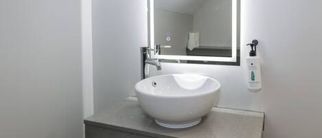 A modern bathroom with a white sink, a large mirror, and a hand sanitizer dispenser.