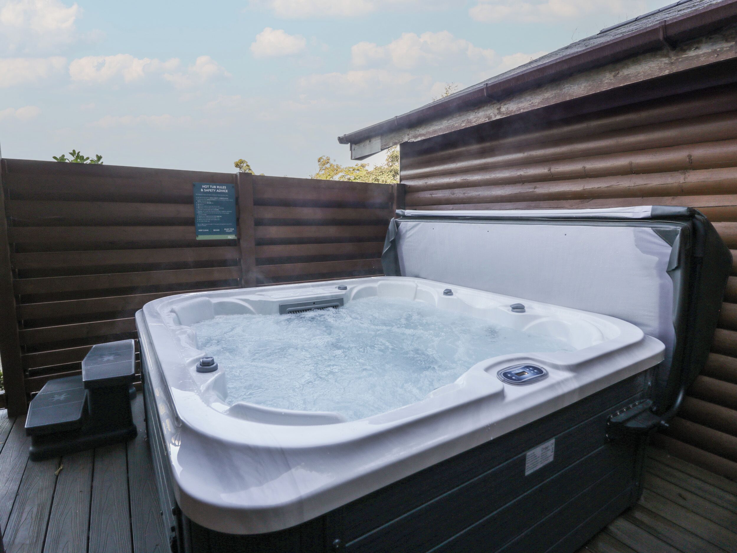 A hot tub in an outdoor setting with a wooden deck and a signboard.