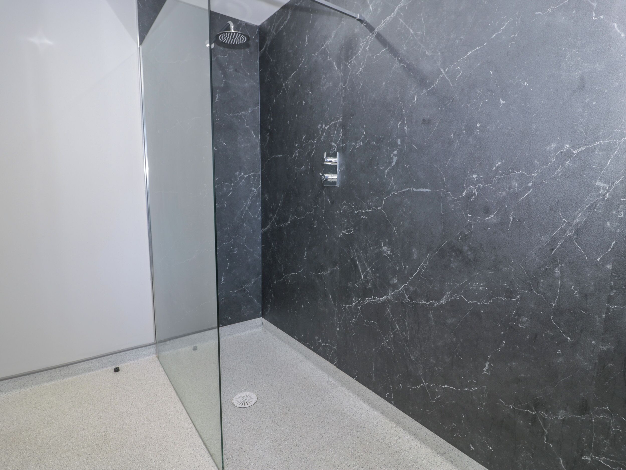 A modern bathroom with a glass-enclosed shower, dark marble walls, and a white floor.