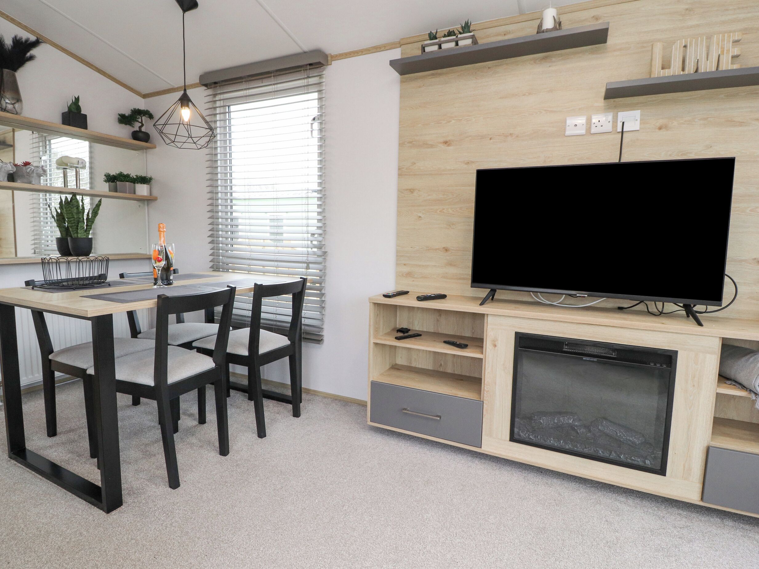 A modern living room with a flat-screen TV, wooden entertainment unit, dining table with chairs, and a fireplace.