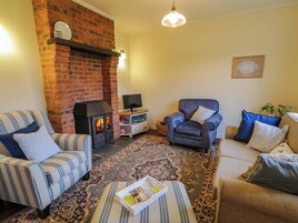 A cozy living room with a brick fireplace, striped sofas, a blue armchair, and a patterned rug.