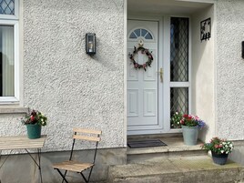 A house with a white door, a wooden chair, and potted plants.