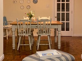 A dining area with a wooden table and four chairs, a vase with flowers, and a door with glass panels.