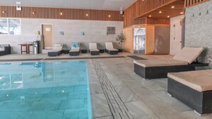 Un espace piscine intérieur moderne, doté de chaises longues et d’une eau cristalline.