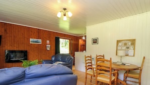 A cozy room with a blue sofa, wooden dining table with chairs, a TV mounted on the wall, and a ceiling light fixture. - Lodge 1 "ash" (Isle of Arran)
