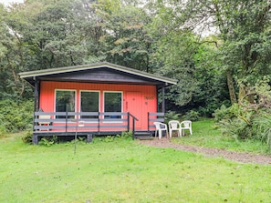 Une petite cabane à l’extérieur rouge, avec une véranda dotée de deux chaises et une terrasse en bois.
