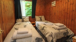 A room with wooden walls and two beds with animal print bedding. - Lodge 1 "ash" (Isle of Arran)