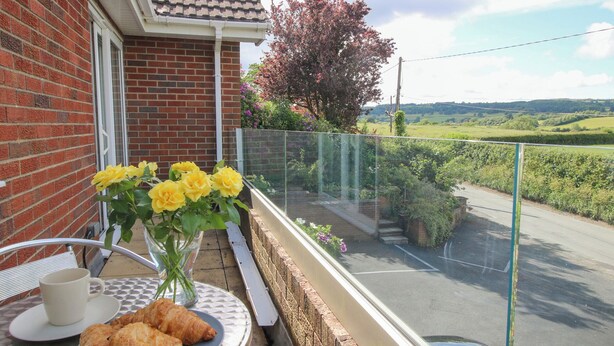 A balcony with a table set for breakfast, including croissants and a cup, overlooking a road and greenery. - Plum Hill (Oswestry)