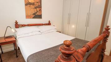 A bedroom with a wooden bed, white bedding, a nightstand, a lamp, and a wardrobe.