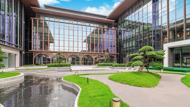 Un bâtiment moderne doté de grandes fenêtres en verre, d’une cour intérieure agrémentée d’un élément aquatique et d’un espace vert bien entretenu.