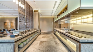 Un hall d’hôtel moderne avec un sol en marbre, un comptoir d’accueil, un espace salon et une cloison en verre.
