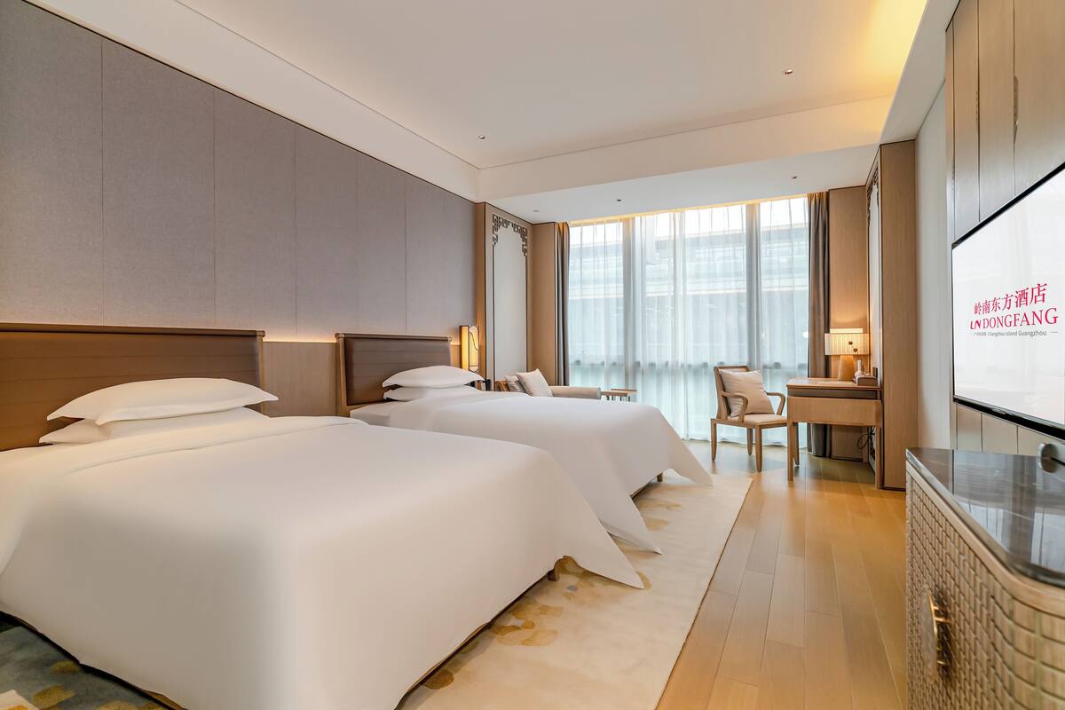 A hotel room with two beds, a desk, a chair, and a TV screen.