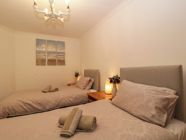 A hotel room with two beds, a chandelier, a nightstand with a lamp, and a wall-mounted painting.