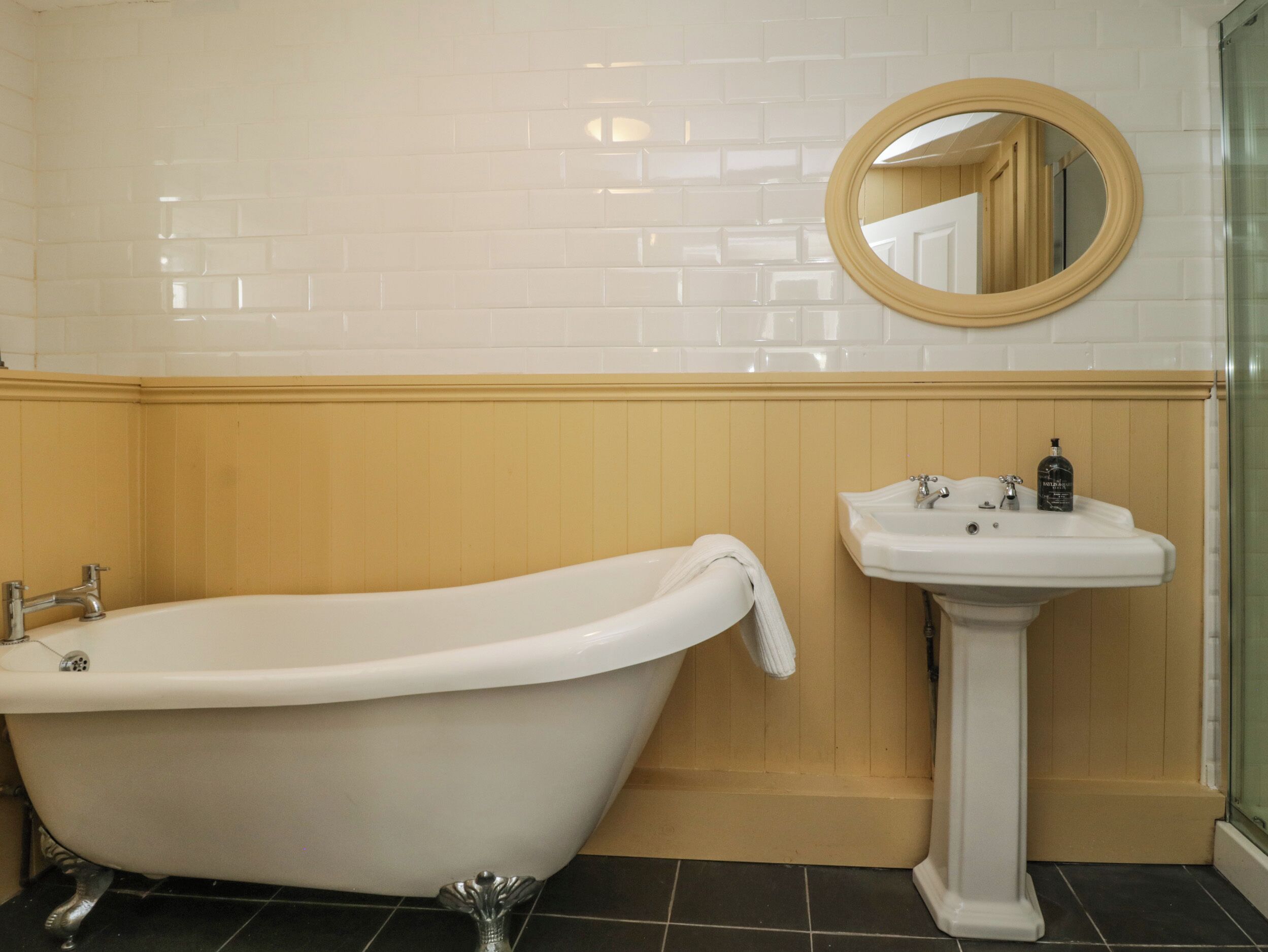 A bathroom with a freestanding bathtub, a pedestal sink, and a round mirror.