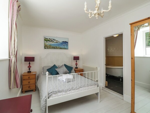 A bedroom with a white bed, two bedside tables with lamps, a painting on the wall, and a view of the bathroom through an open door.