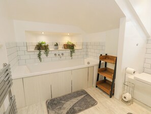A modern bathroom with a large bathtub, a double sink, and a wooden shelf unit.