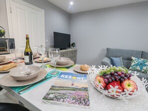 A dining area with a table set for two, a bottle of wine, glasses, plates, and a basket of fruit.