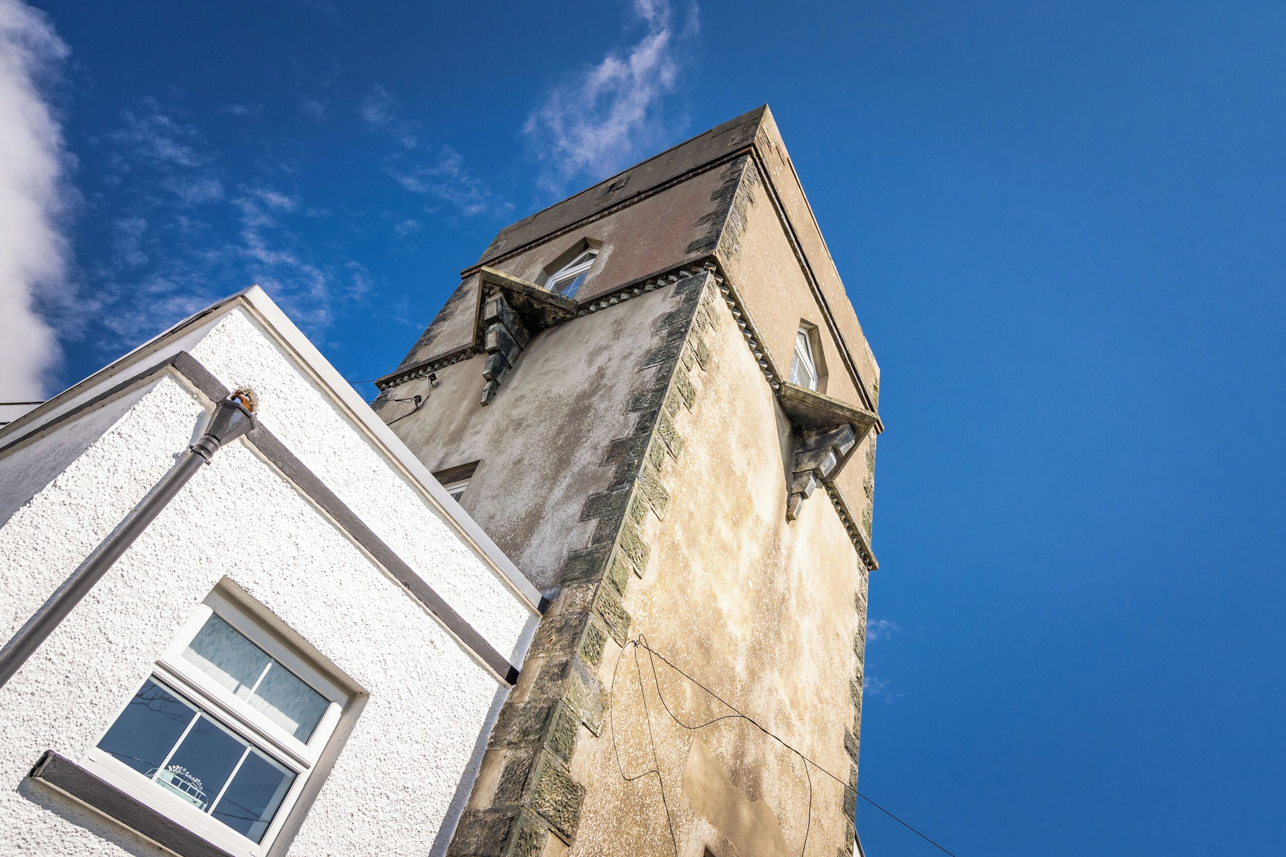 A corner of a building with a white facade and a corner tower with a dark roof.