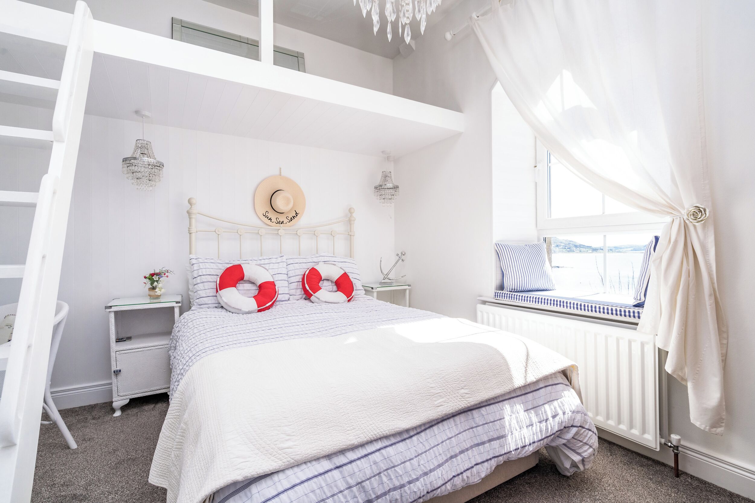 A bedroom with a bed, a nightstand, a window with a view, a chandelier, and a white ceiling.
