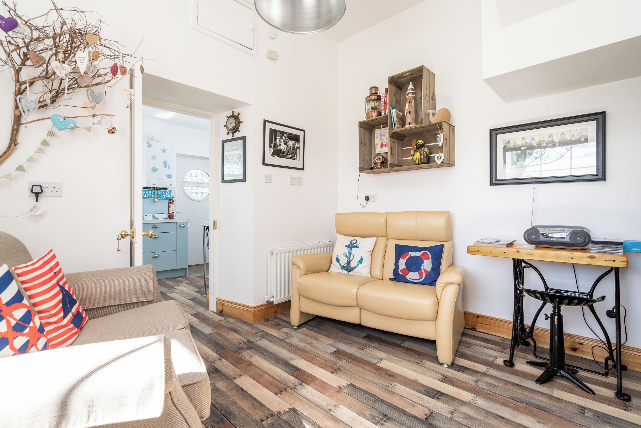Una sala de estar acogedora con un sofá color beige, una mesa de centro de madera y un radiador. En la pared hay cuadros enmarcados y un estante con objetos decorativos.
