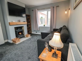 Una sala de estar con chimenea, un sofá, una mesa con lámpara y un televisor montado en la pared.