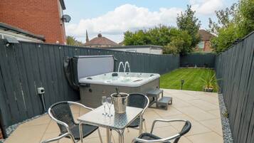 An outdoor patio with a hot tub, a table, and four chairs.